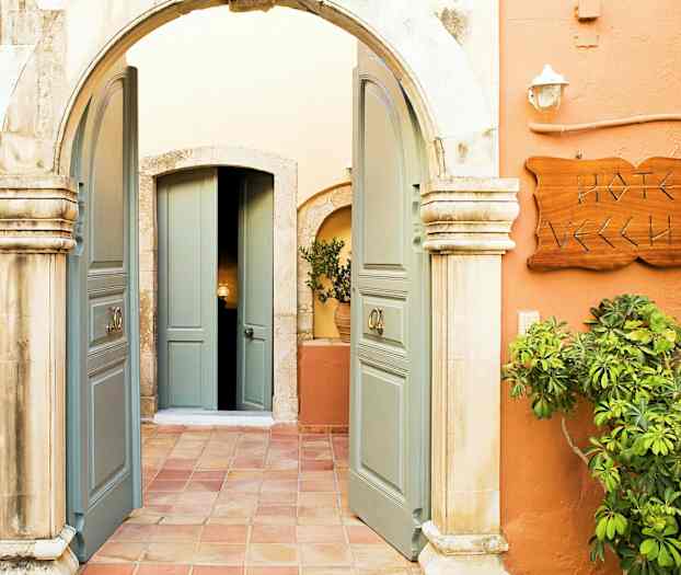 Bildet viser en inngang med en bue, åpne doble dører, et skilt som sier 'Hotel Vecchio' og vegetasjon rundt. (AI-generert tekst)