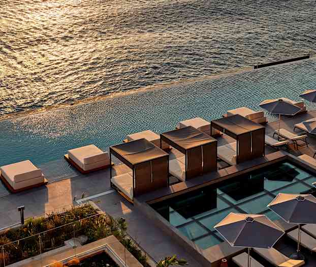 Utsikt over solsenger og skjermende parasoller ved et infinitybasseng med havet i bakgrunnen. (AI-generert tekst)