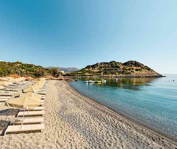 En strand med solsenger og parasoller ved en rolig bukt. (AI-generert tekst)