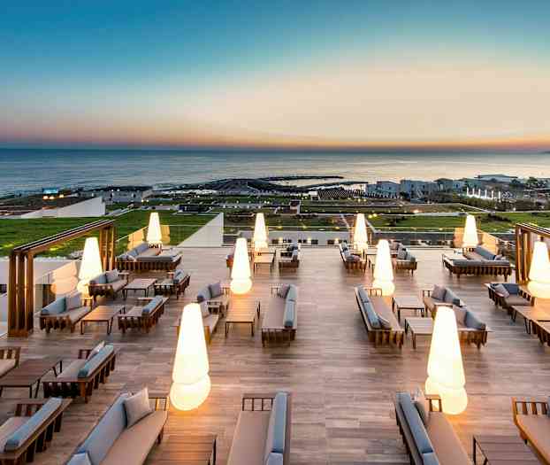 Moderne utemøbler med opplyste lamper på en stor terrasse med havutsikt. (AI-generert tekst)