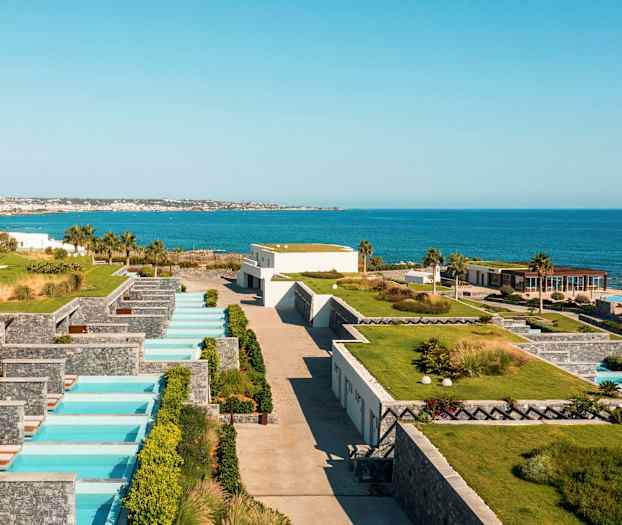 Utsikt over en ferieanlegg ved sjøen med private bassenger og grøntområder. (AI-generert tekst)