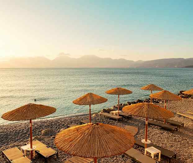 Strand med solsenger og parasoller, med utsikt over havet ved solnedgang. (AI-generert tekst)