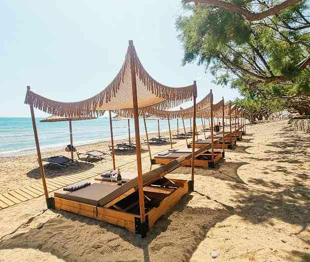 Bilde av en sandstrand med solsenger og treparasoller. (AI-generert tekst)