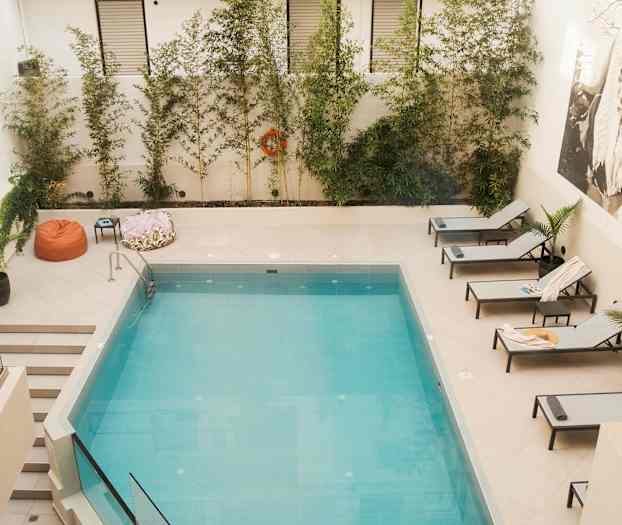 Et svømmebasseng med solsenger og vegetasjon rundt. (AI-generert tekst)