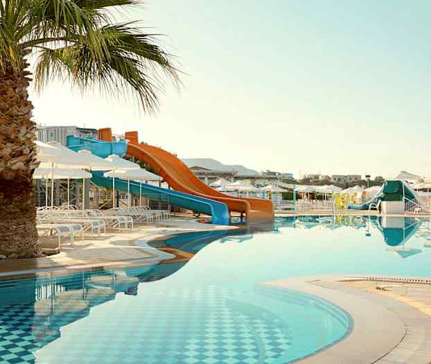 Bilde av et basseng med vannsklier og solsenger, samt en palme i forgrunnen. (AI-generert tekst)