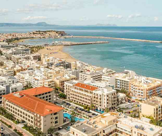 Flyfoto av en kystby med sandstrand og båthavner. (AI-generert tekst)