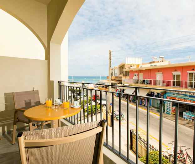 En balkong med bord og stoler, med utsikt over gaten og havet. (AI-generert tekst)