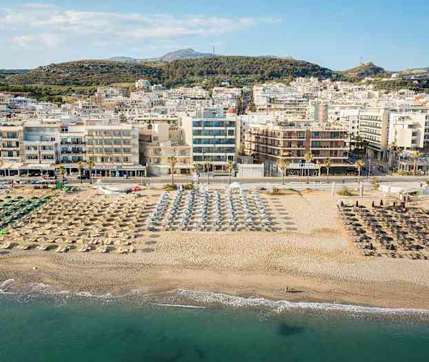 Utsikt over en strand med parasoller og solsenger, og en by i bakgrunnen. (AI-generert tekst)