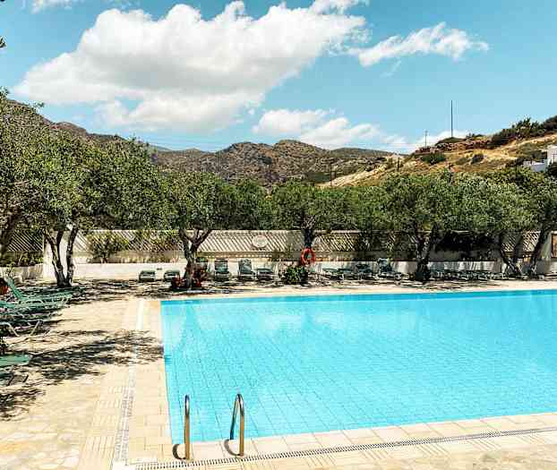 Et utendørs basseng omgitt av solsenger og trær under en klar himmel. (AI-generert tekst)