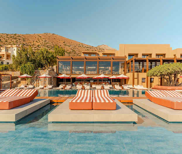 Et luksuriøst hotellkompleks med basseng, solsenger og en fjellrik bakgrunn. (AI-generert tekst)