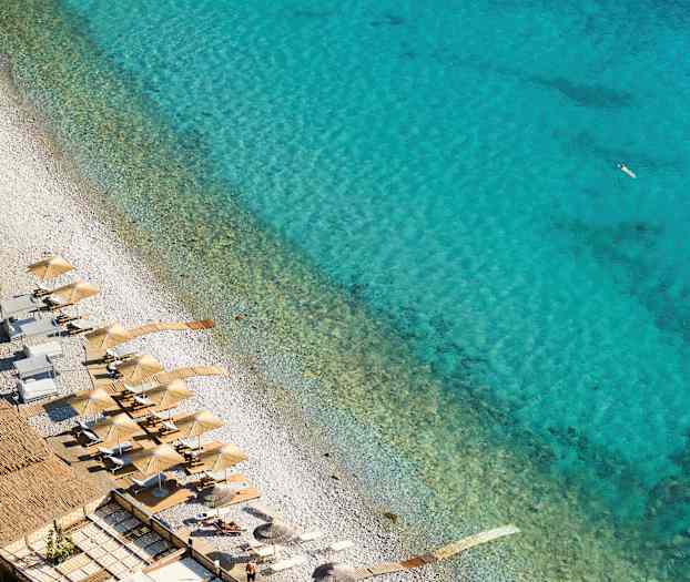 Utsikt over en strand med parasoller og solsenger ved klart blått vann. (AI-generert tekst)