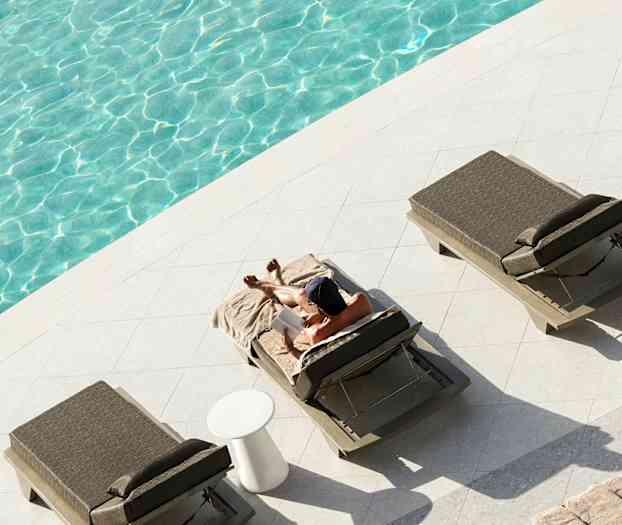 En person slapper av på en solseng ved siden av et basseng. (AI-generert tekst)