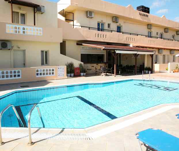 Et utendørsbasseng ved et hotell med solsenger og bygningen i bakgrunnen. (AI-generert tekst)