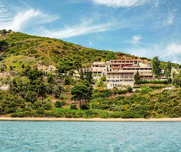 Hotellkompleks ved en grønnkledd skråning nær vann. (AI-generert tekst)