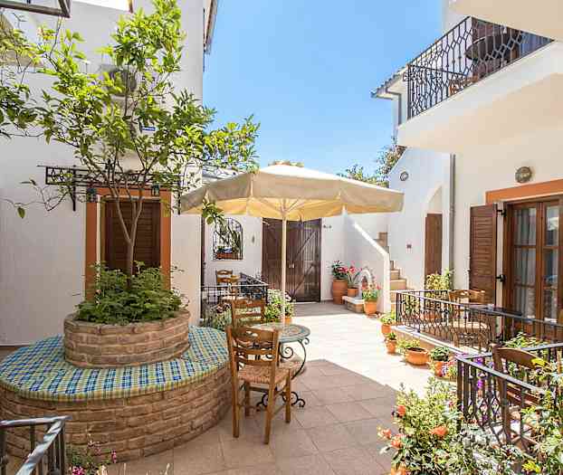 Inngårdsplass med blomsterpotter, trær og utemøbler under en parasoll. (AI-generert tekst)