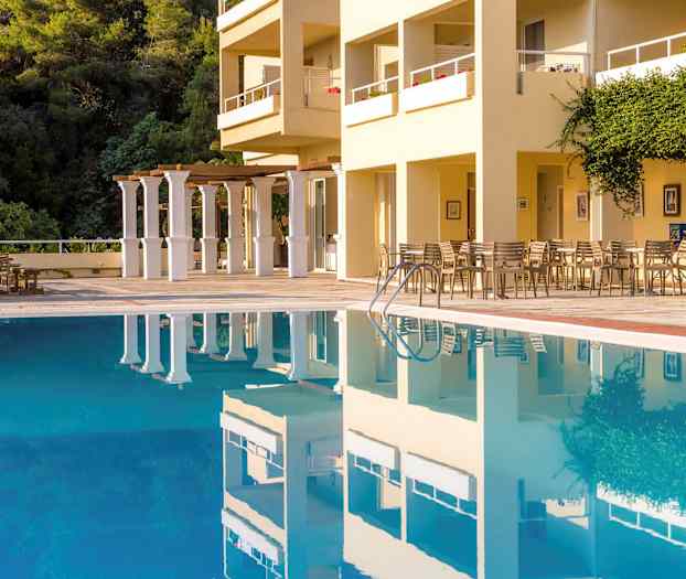 Et utendørs basseng foran en bygning med sitteplasser og vegetasjon. (AI-generert tekst)