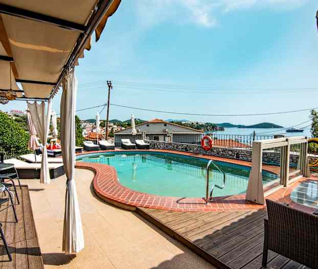 Et basseng med omkringliggende solsenger og utsikt over havet. (AI-generert tekst)