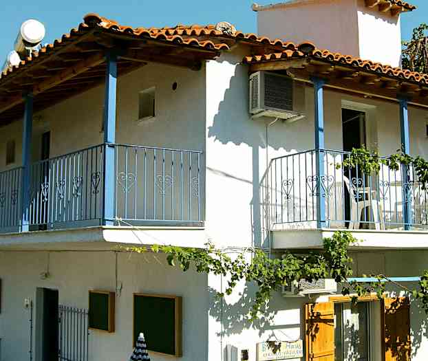 En toetasjes bygning med hvit fasade, blå balkonger og røde takstein. (AI-generert tekst)