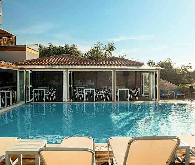 Utendørs svømmebasseng med solsenger og en restaurant i bakgrunnen. (AI-generert tekst)