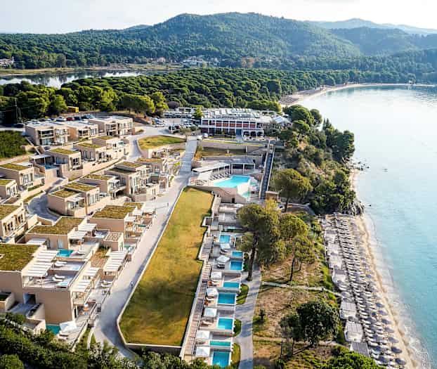 Flyfoto av et strandnært hotell med bassenger og solsenger. (AI-generert tekst)