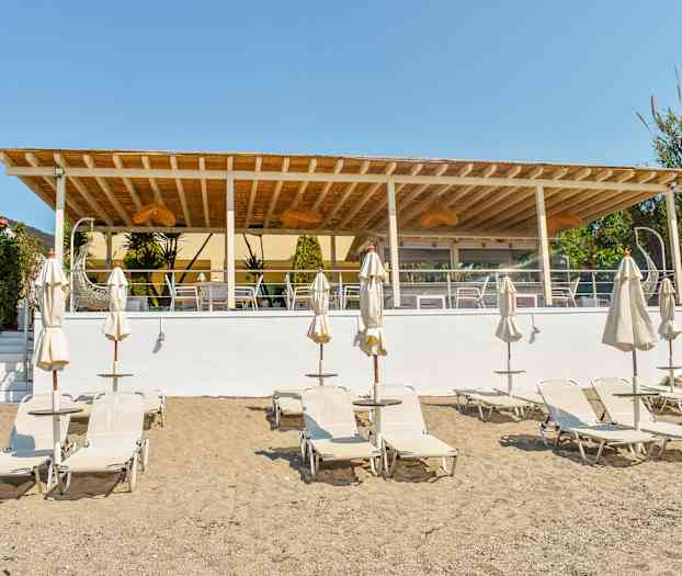 Strand med solsenger og parasoller foran en utendørs terrasse. (AI-generert tekst)