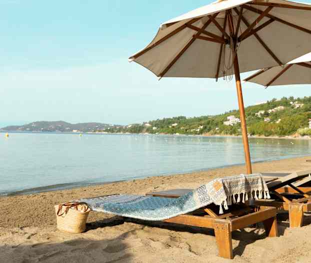 Strand med solsenger og store parasoller samt havutsikt. (AI-generert tekst)