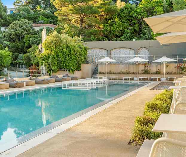 Et utendørs svømmebasseng med solsenger og parasoller og omkringliggende grøntområder. (AI-generert tekst)