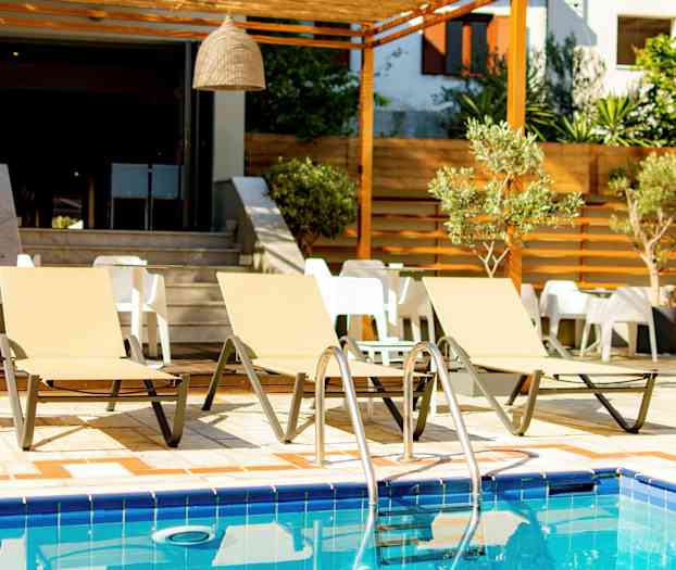 Tre solsenger ved et basseng med bord og stoler i bakgrunnen. (AI-generert tekst)