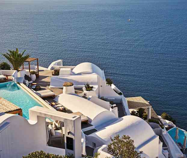 Et hvitt feriekompleks med et basseng og utsikt over det blå havet. (AI-generert tekst)