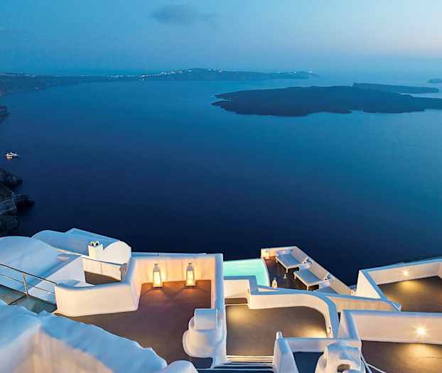 En utsikt ved skumringen med hvite bygninger nær vann og fjell. (AI-generert tekst)