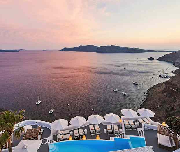 En utsikt over en kystlinje med havet ved solnedgang. I forgrunnen er et basseng og hvite solsenger med parasoller. (AI-generert tekst)