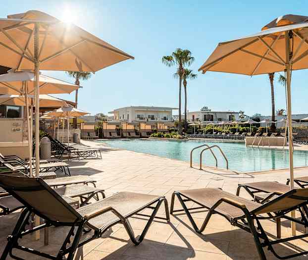 Bilde av et bassengområde med solsenger og parasoller, og bygninger i bakgrunnen. (AI-generert tekst)