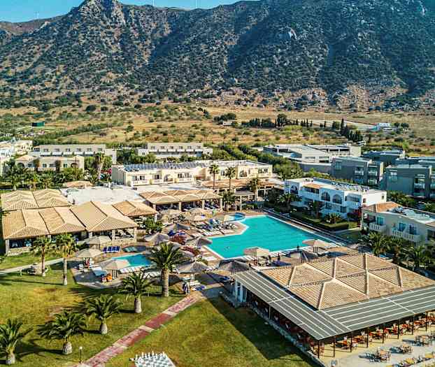 Bilde av et feriehotell med basseng og omliggende bygninger, plassert nær et fjellandskap. (AI-generert tekst)