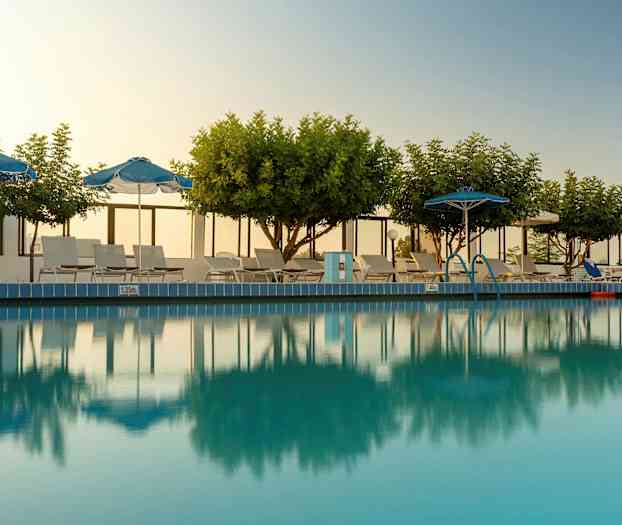 Utendørsbasseng med trær, parasoller og solsenger rundt. (AI-generert tekst)