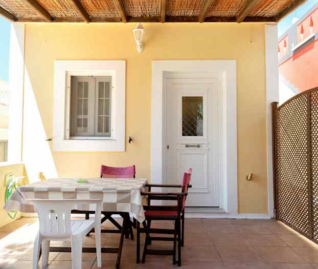 En uteplass med et bord og stoler foran en dør og et vindu. (AI-generert tekst)