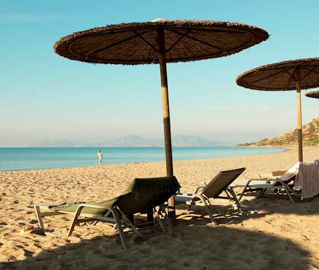 En sandstrand med parasoller og solstoler ved sjøen. (AI-generert tekst)