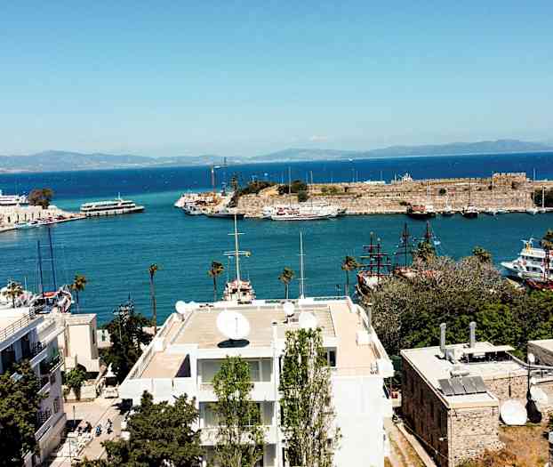 Utsikt over et havneområde med båter og en historisk bygning ved kysten. (AI-generert tekst)