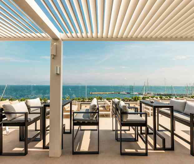 Utendørs servering med utsikt over havet, med sofaer og bord under en pergola. (AI-generert tekst)