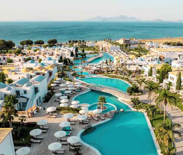 Utsikt over en ferieby med bassenger, hvite bygninger og havutsikt i bakgrunnen. (AI-generert tekst)