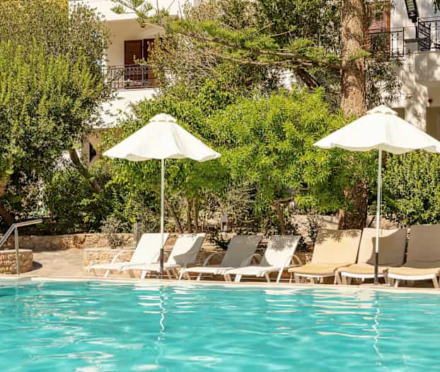 Et utendørs basseng med solsenger og parasoller omgitt av frodig vegetasjon. (AI-generert tekst)