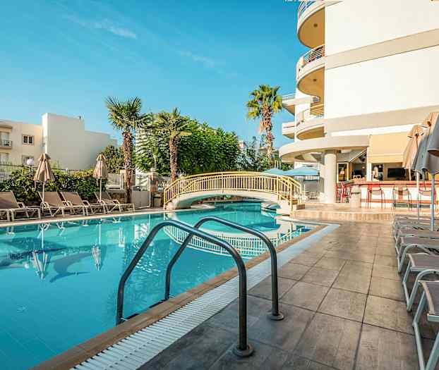 Et utendørsbasseng med solsenger og parasoller ved siden av, samt en liten bro over bassenget. (AI-generert tekst)