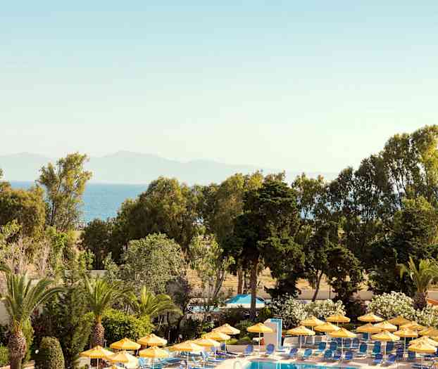 Bassengområde med gule parasoller omgitt av grøntområder og utsikt mot havet. (AI-generert tekst)