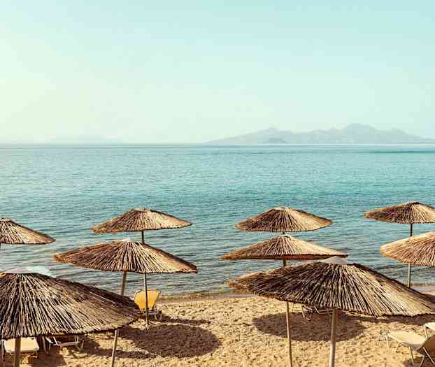 Strand med parasoller av halm ved sjøen. (AI-generert tekst)