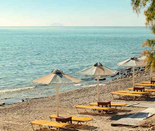 Solstoler og parasoller på en sandstrand med utsikt over havet. (AI-generert tekst)