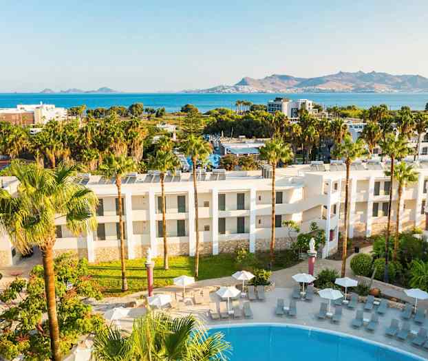 Hotellets utside med bassengområde og utsikt mot havet og fjellene. (AI-generert tekst)