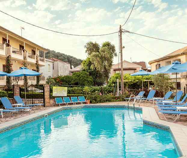 Et basseng omgitt av solsenger og parasoller, med bygninger og trær i bakgrunnen. (AI-generert tekst)