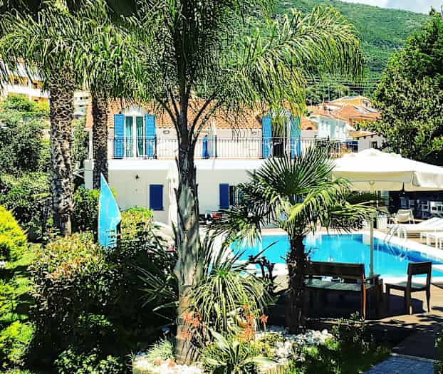 En hage med palmer og planter rundt et basseng foran en lys bygning. (AI-generert tekst)