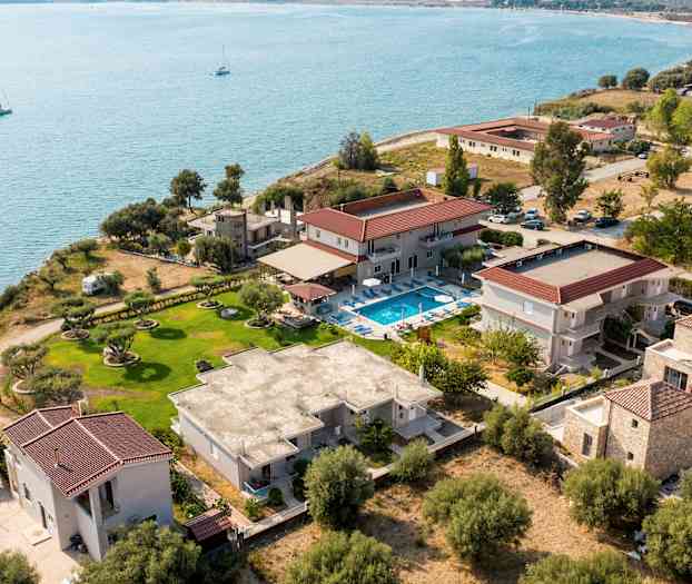 Fugleperspektiv av en kysteiendom med ulike bygninger, en plen og et basseng nær vannet. (AI-generert tekst)