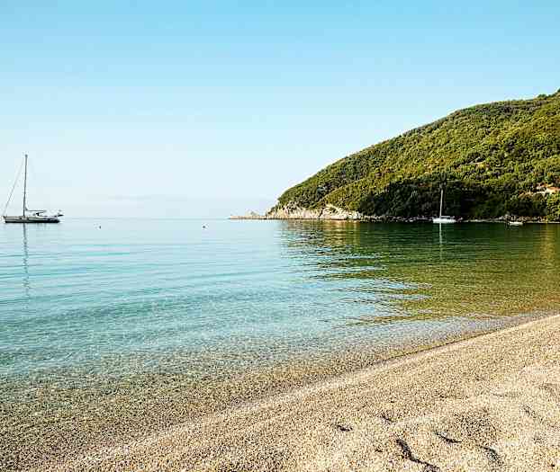 En rolig strand med klart vann og seilbåter i det fjerne. (AI-generert tekst)