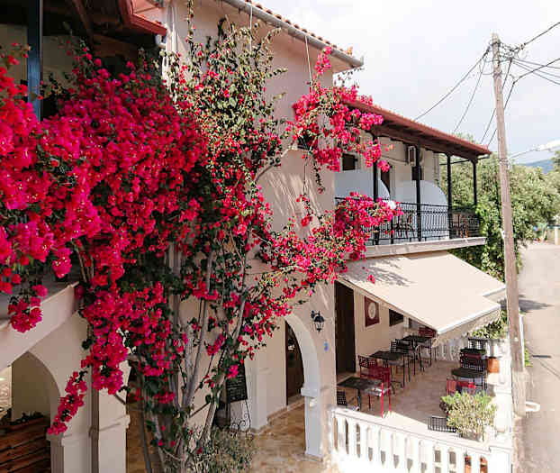 Et hus med røde blomster som klatrer på fasaden og en terrasse med møbler ved siden av en liten vei. (AI-generert tekst)